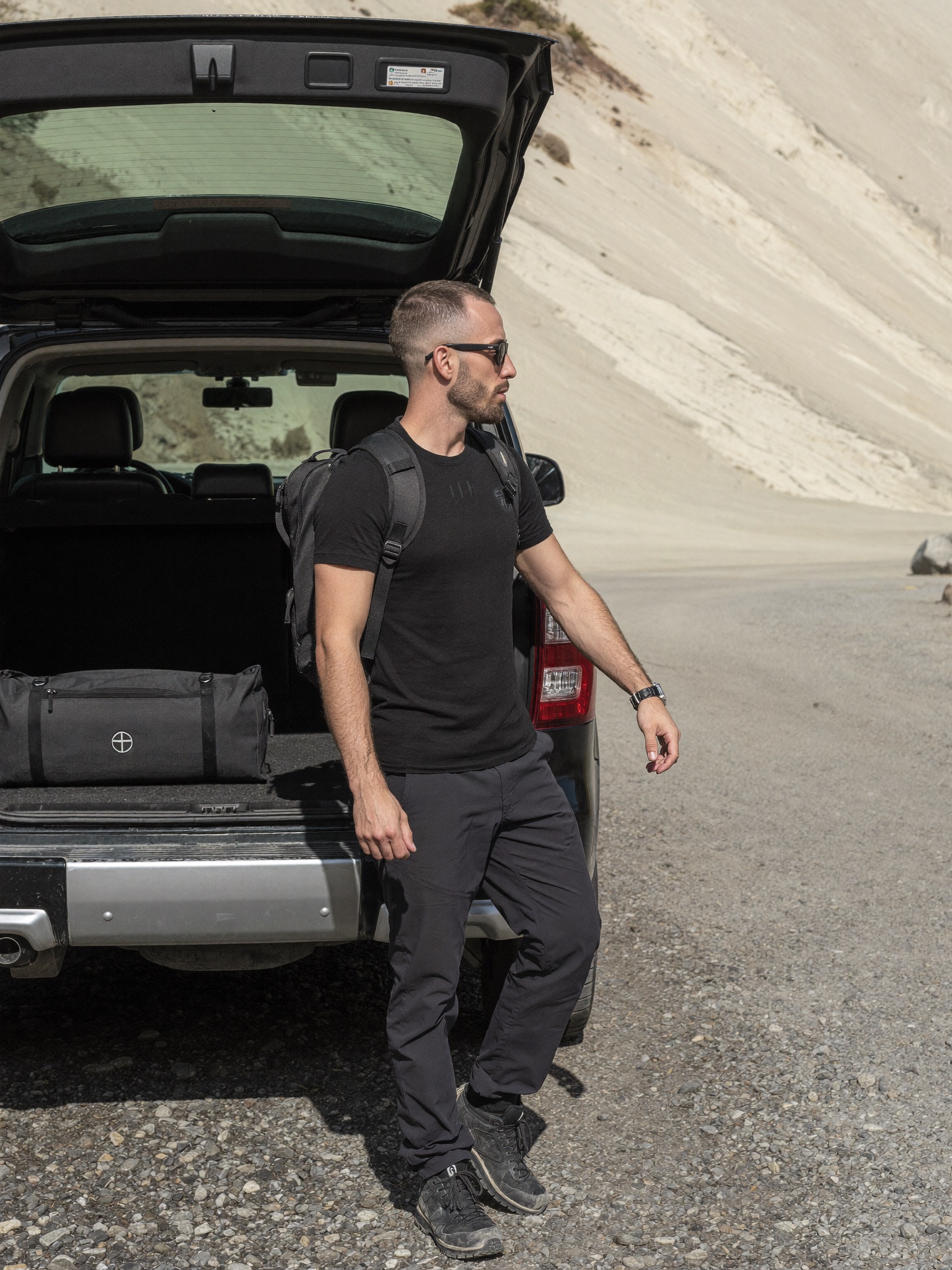 Cody Wise standing at a remote mountain trailhead beside a parked vehicle in midday light.