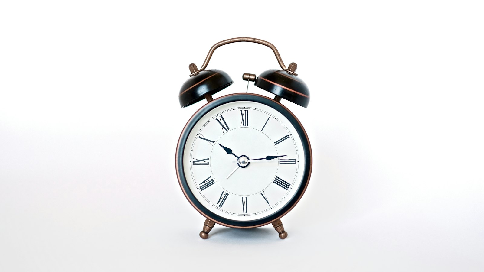 Analog alarm clock on a white surface, illustrating scheduled AI agents all set to fire at the same hour