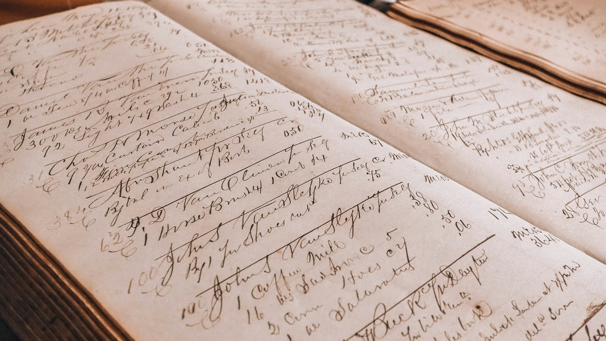 An open ledger filled with handwritten entries beside a glass inkwell on a worn wooden surface.