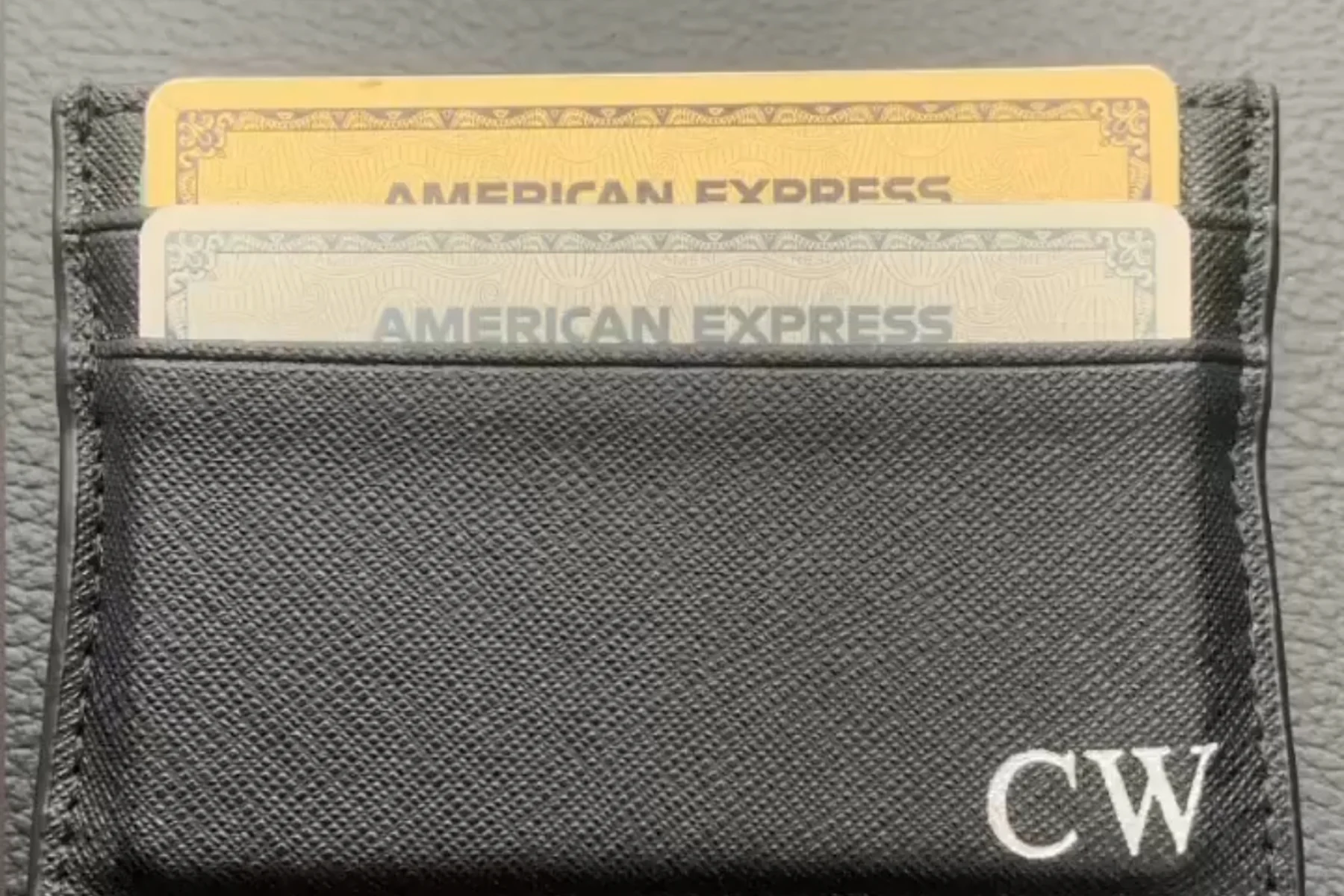 A black leather card holder monogrammed CW, lying flat, with an American Express Gold and an American Express Platinum card in the top slot, each showing the wordmark and none of the card face