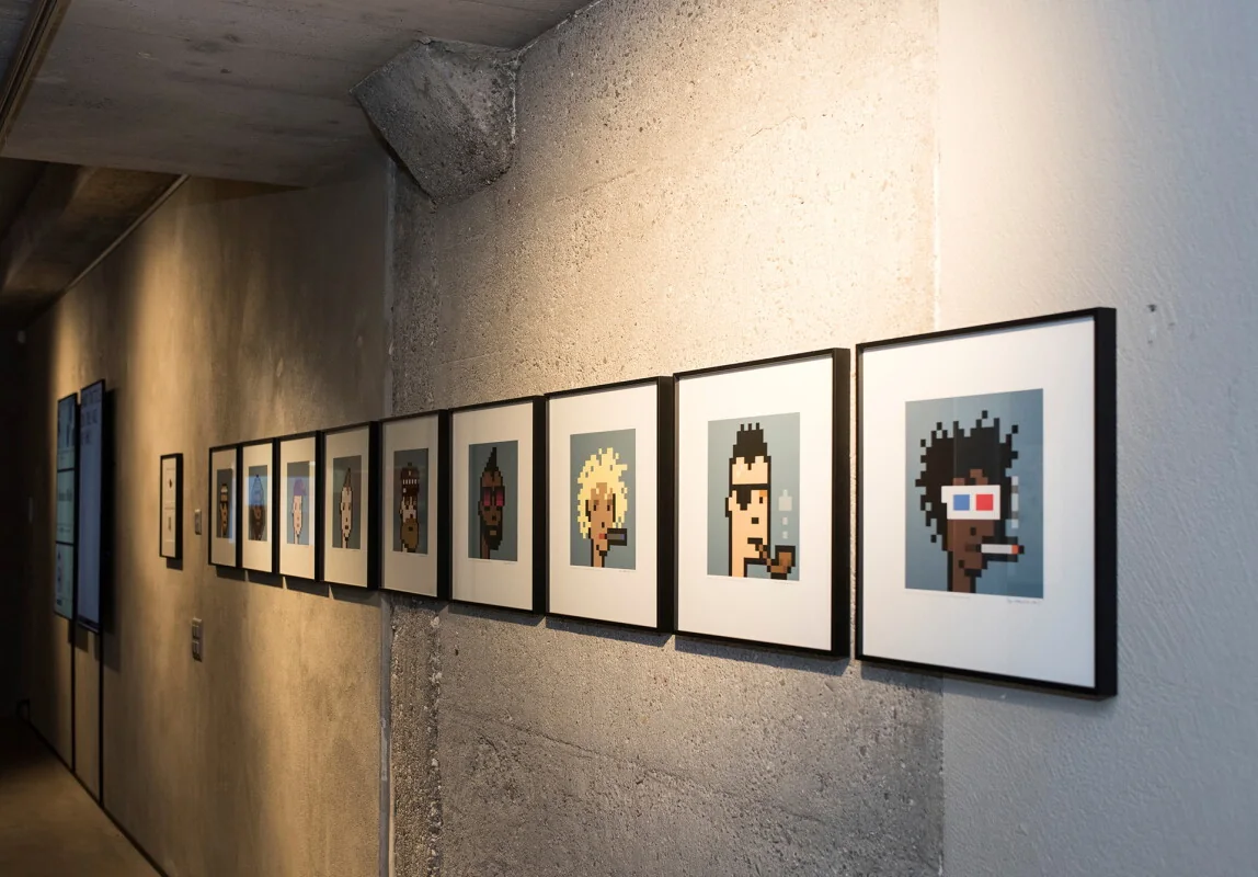 A row of framed CryptoPunk prints hung along a bare concrete gallery wall