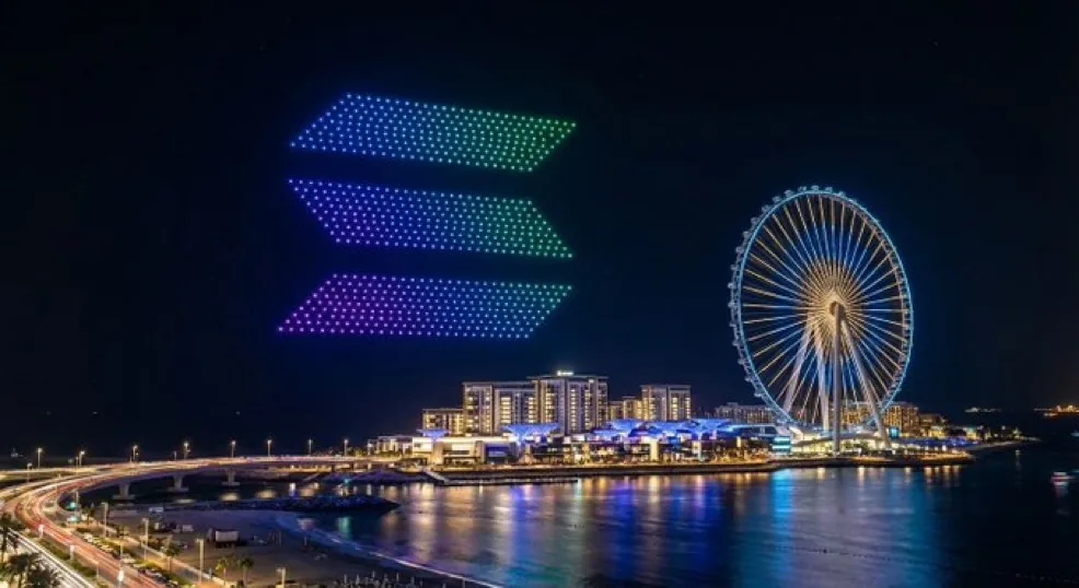 A drone formation of the Solana three bar mark in the night sky over Bluewaters Island in Dubai, with the Ain Dubai observation wheel lit up beside it