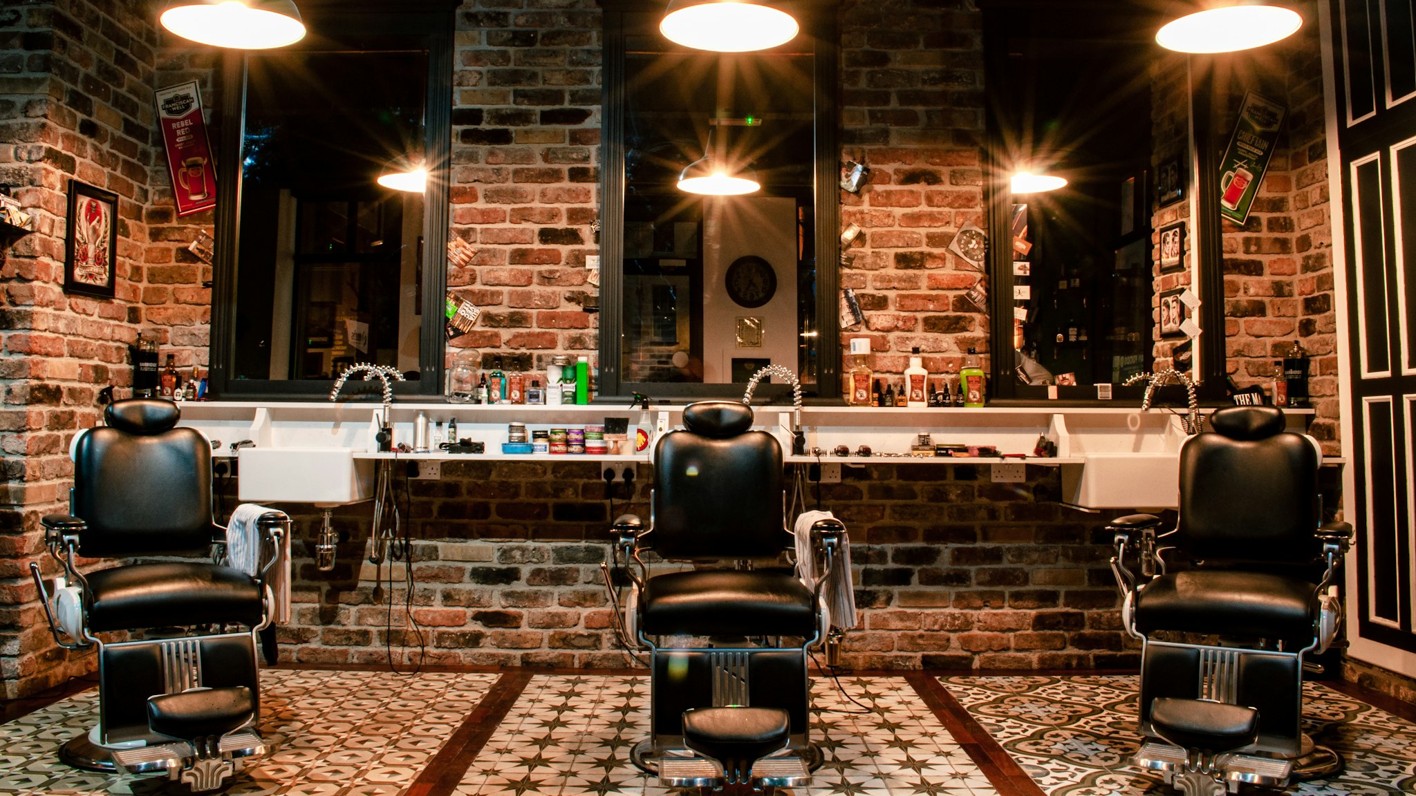 An empty black leather barber chair standing against a brown brick wall
