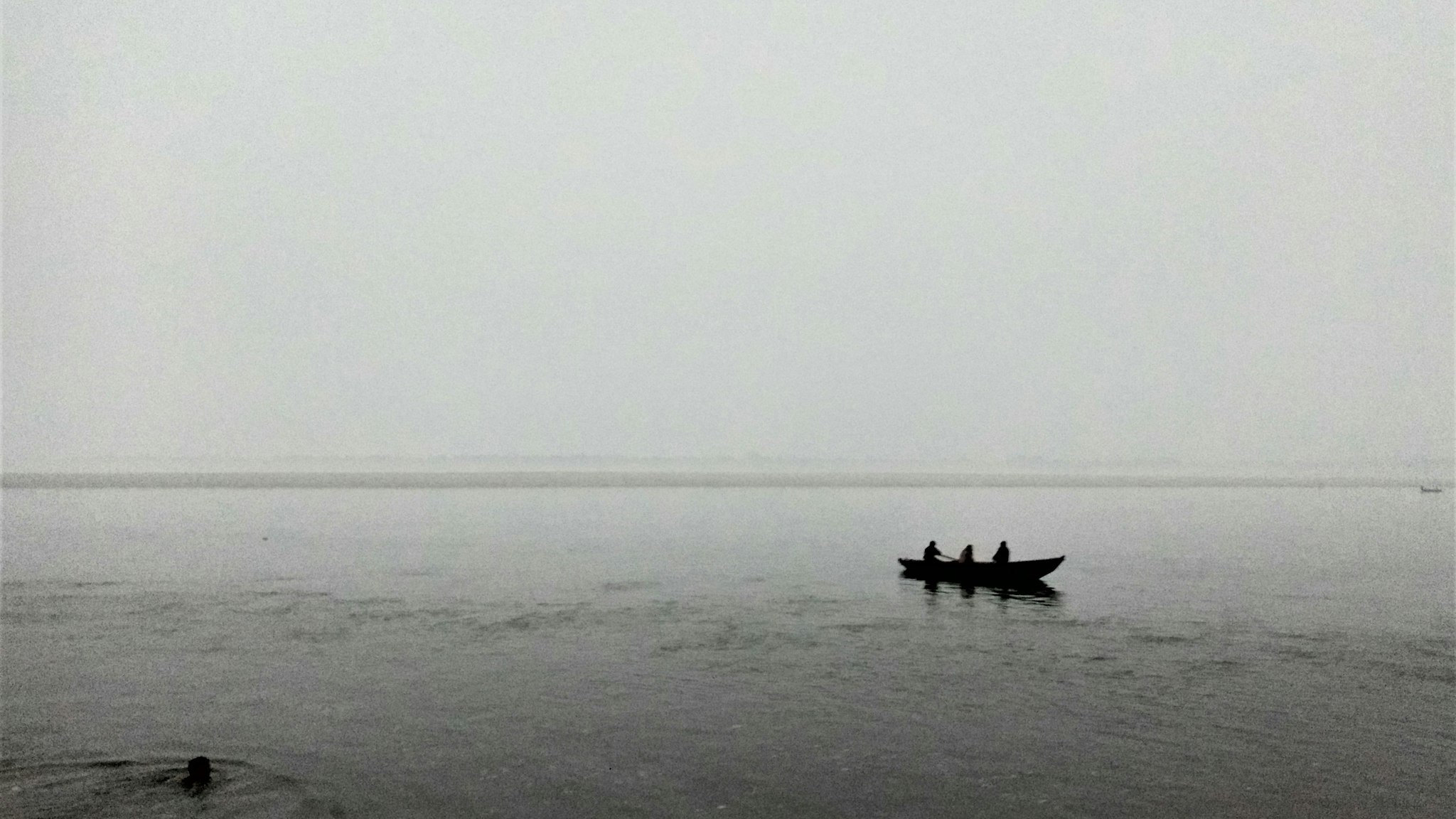 A small open boat carrying figures across flat water in heavy fog with no shoreline visible.