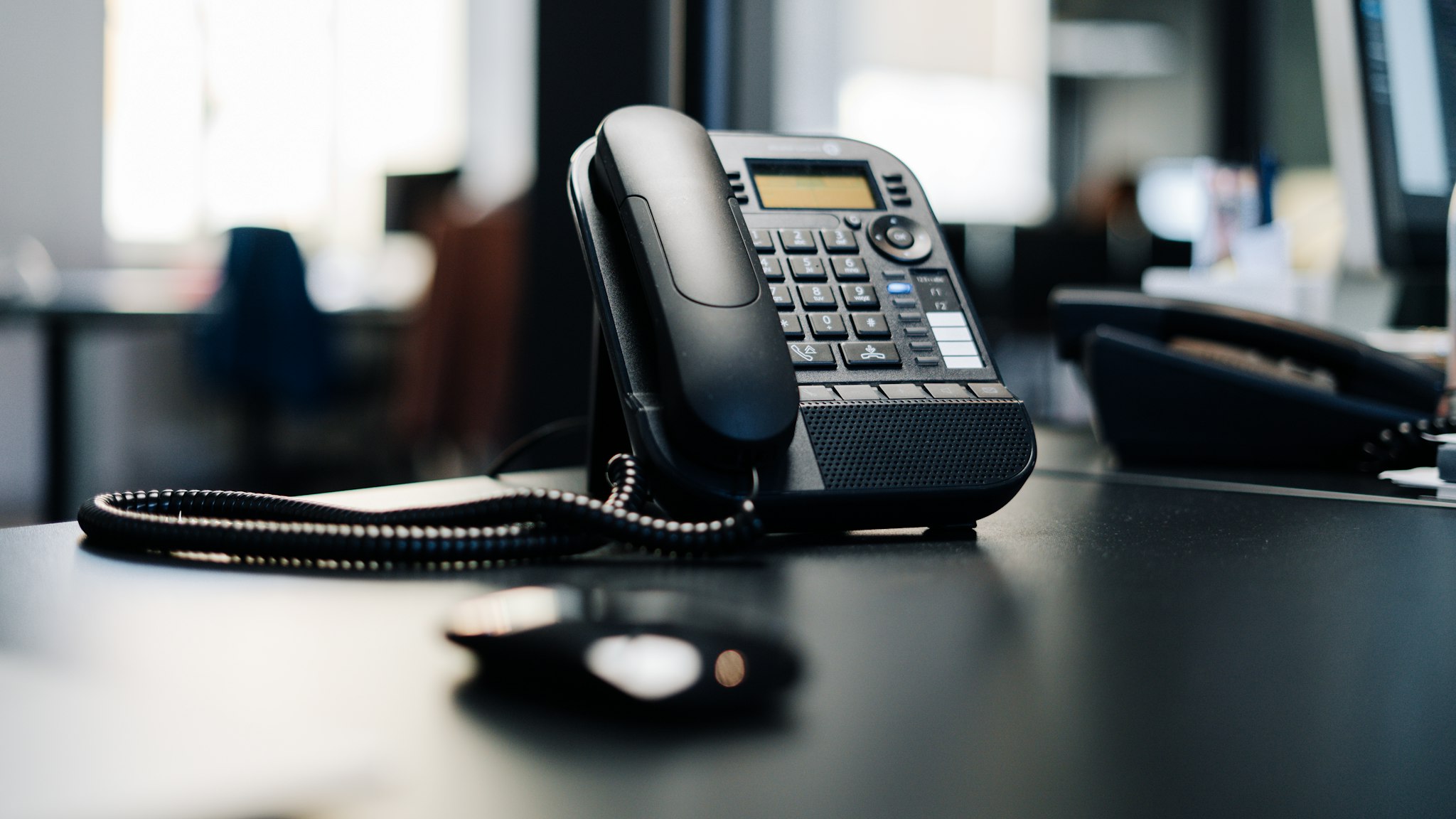 A black desk telephone on a dark wooden office table