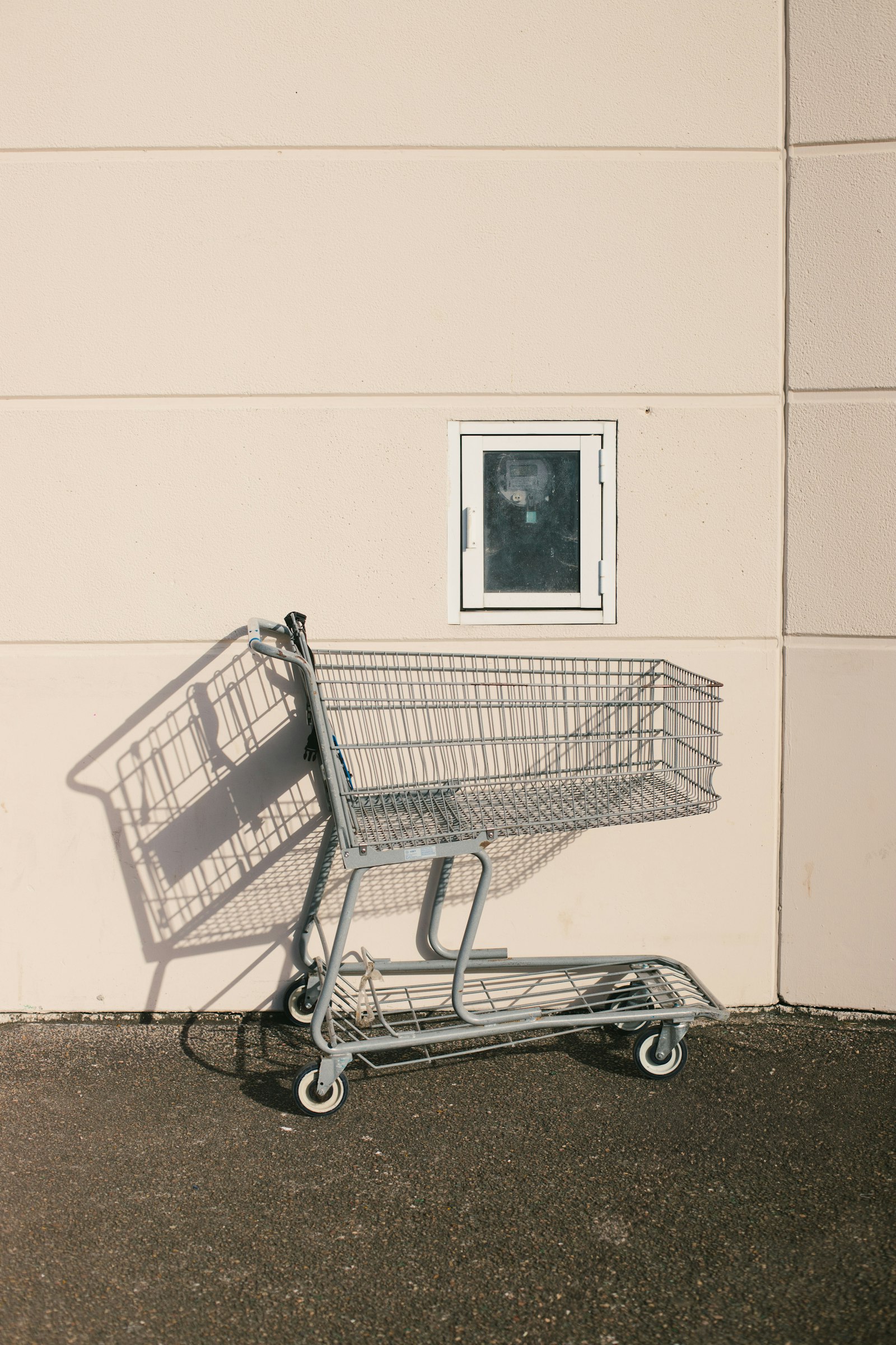 Empty shopping cart against a sunlit wall, casting a long shadow.