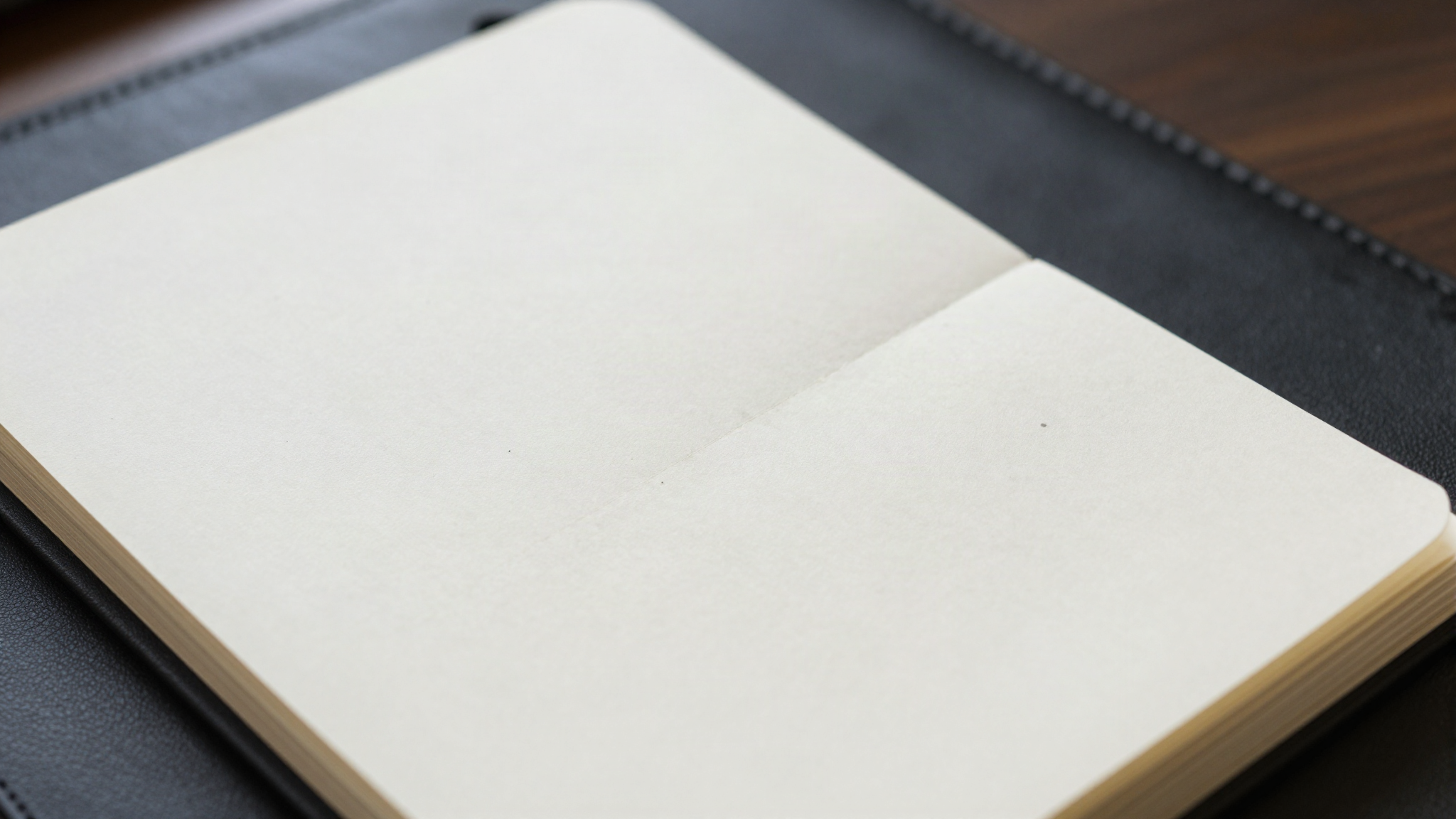 A worn pocket notebook with soft rounded corners and faint pencil marks on a leather desk blotter