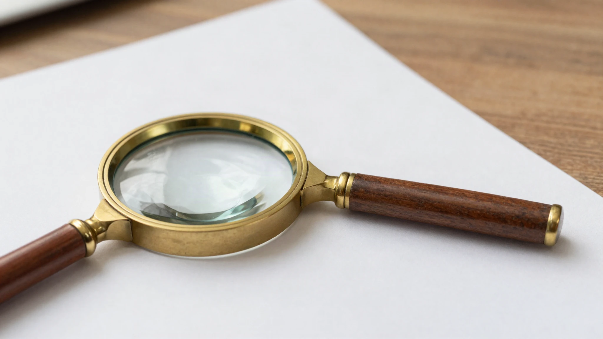 A brass magnifying glass resting on an open printed document on a wooden desk