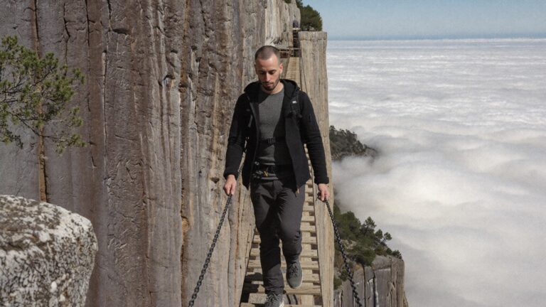 Cody Wise walking a plank path bolted into a sheer cliff face, the wall in the way turned into the way through