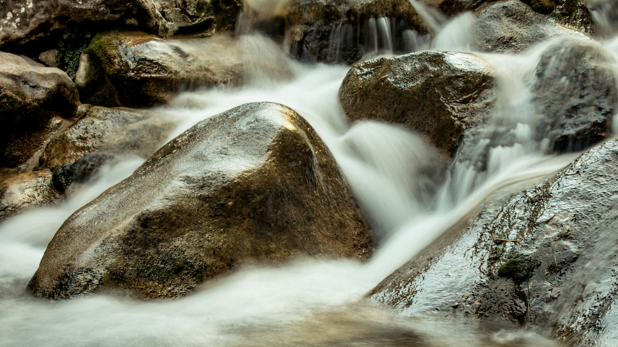 A mountain stream pouring around boulders, the rock in the way becoming the shape of the current