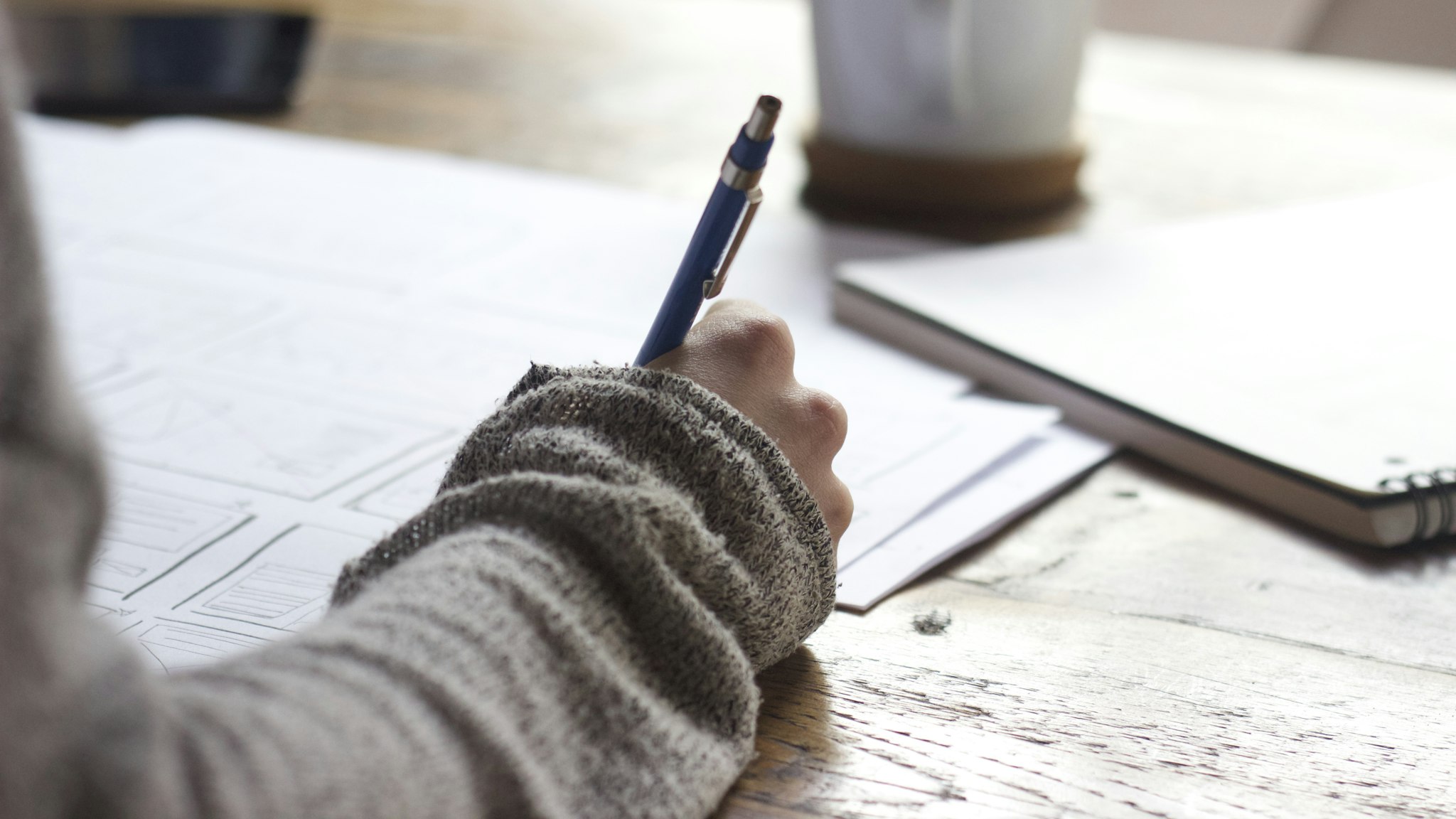 Writing by hand at a table, drafting the page the OTA will never write